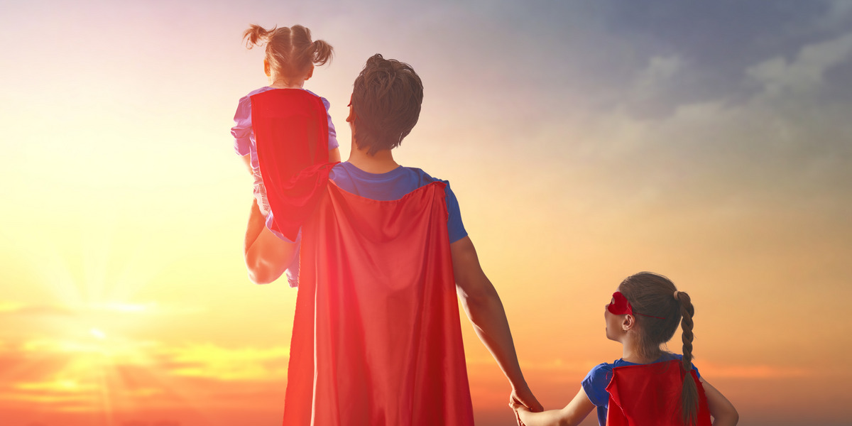 Ein als Superheld verkleideter Mann blickt mit Kindern in einen Sonnenuntergang