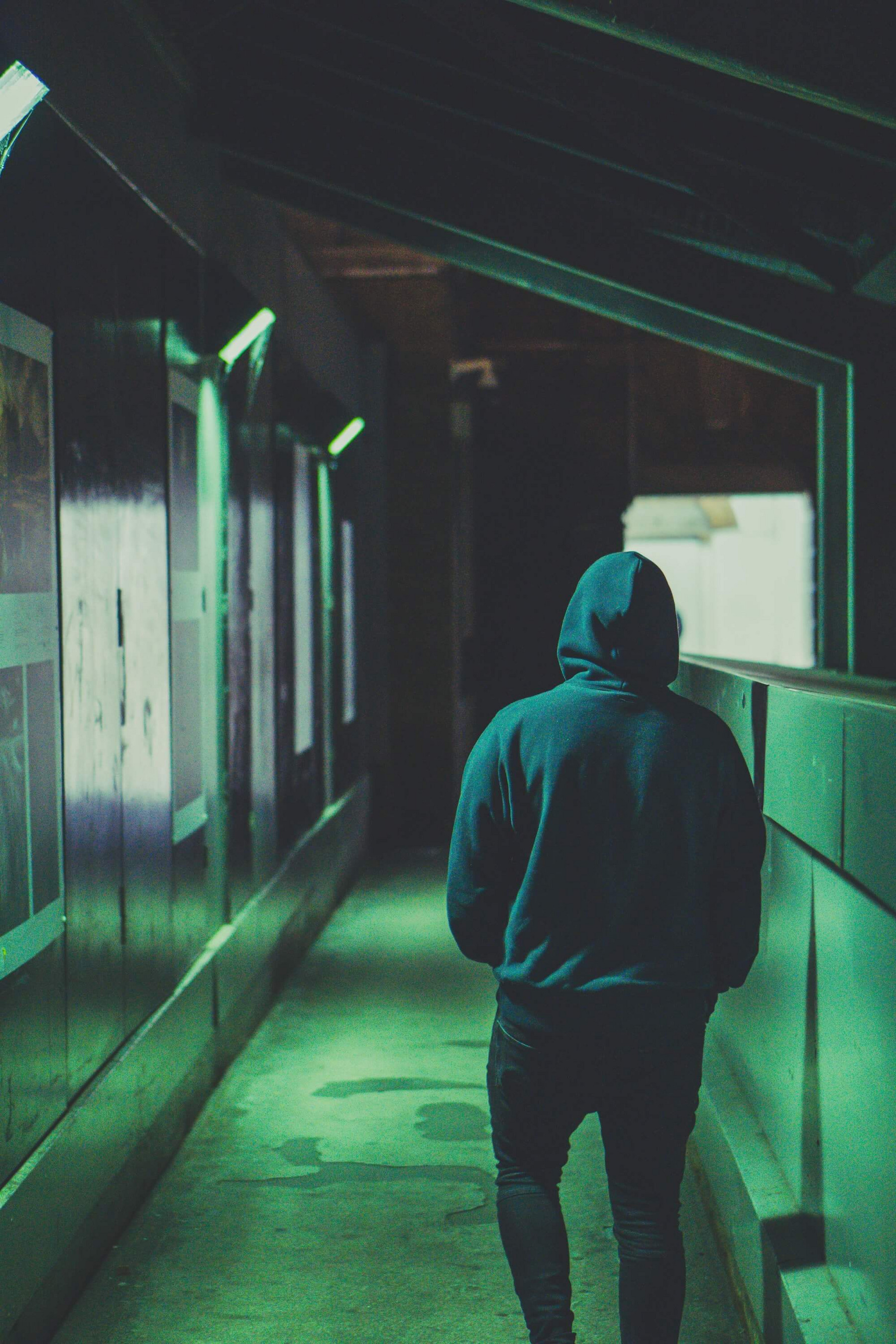 Ein junger Mensch hat sich die Kapuze seines Hoodies übergezogen und läuft vom künstlichen Licht der Lampen beschienen durch einen Bahnhof