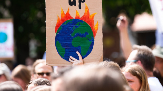 Eine Person auf einer Demo hält einen Schild mit einem brennenden Globus hoch.