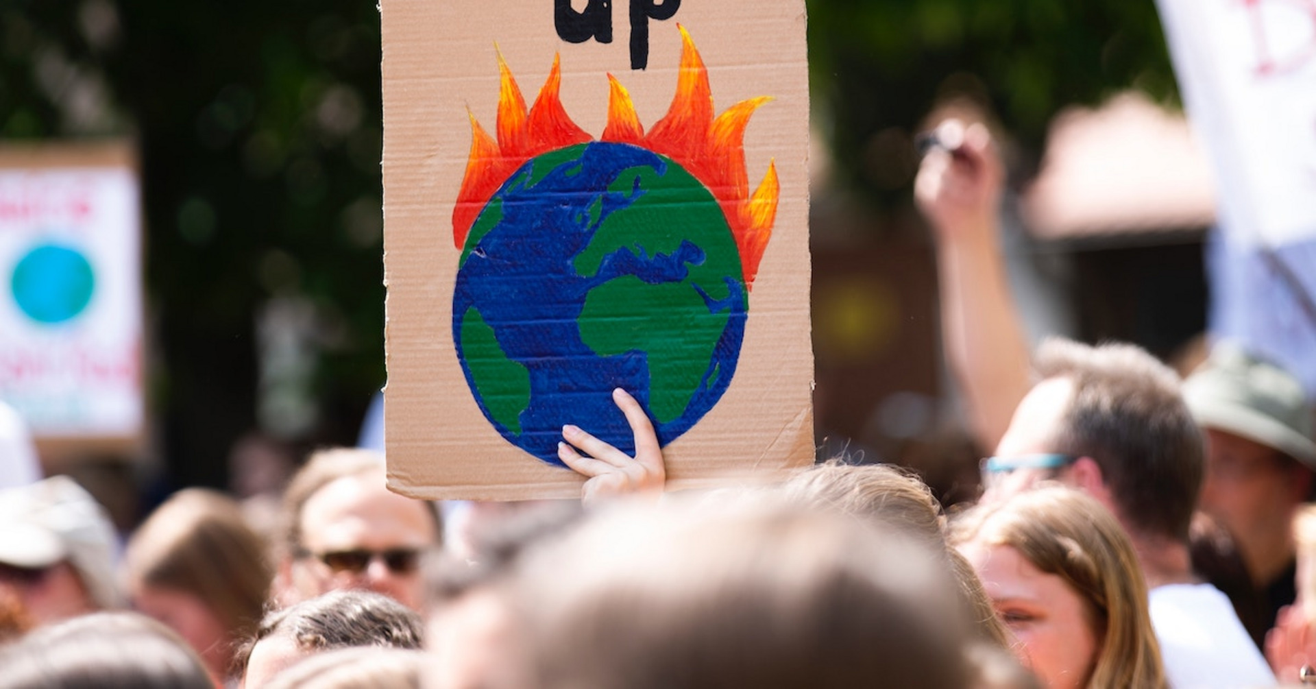 Eine Person auf einer Demo hält einen Schild mit einem brennenden Globus hoch.