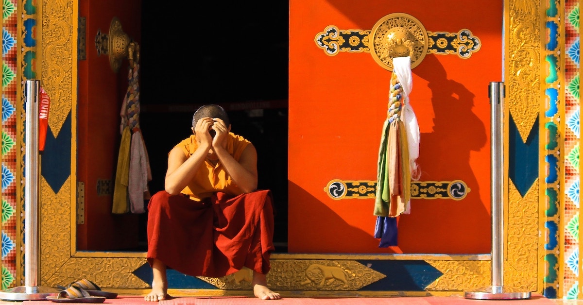 Eine Person mit orangen Klamotten sitzt auf dem Absatz eines Tempels