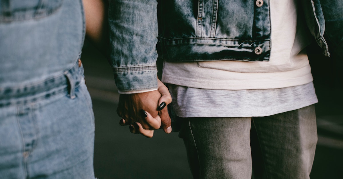 Zwei Personen mit Denim-Klamotten halten Händchen.