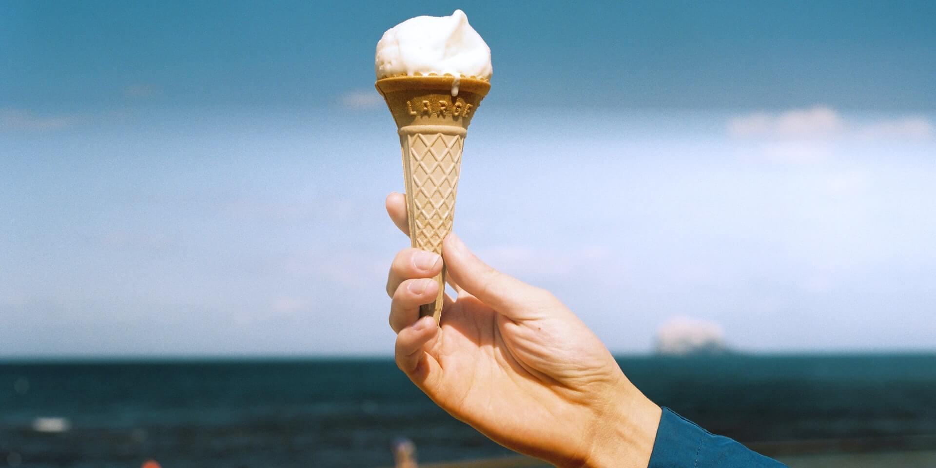 Eine Hand hält eine Eiswaffel Strand.