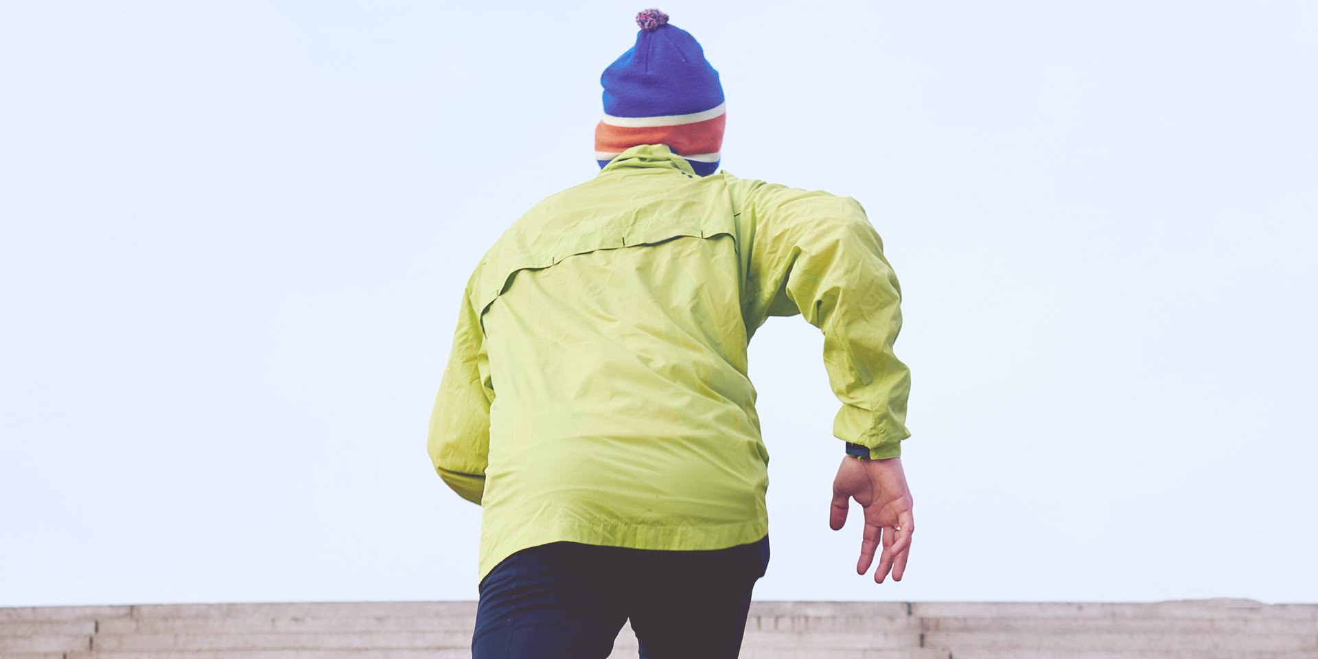 Ein Mann in einer gelben Funktionsjacke joggt eine Treppe hoch.