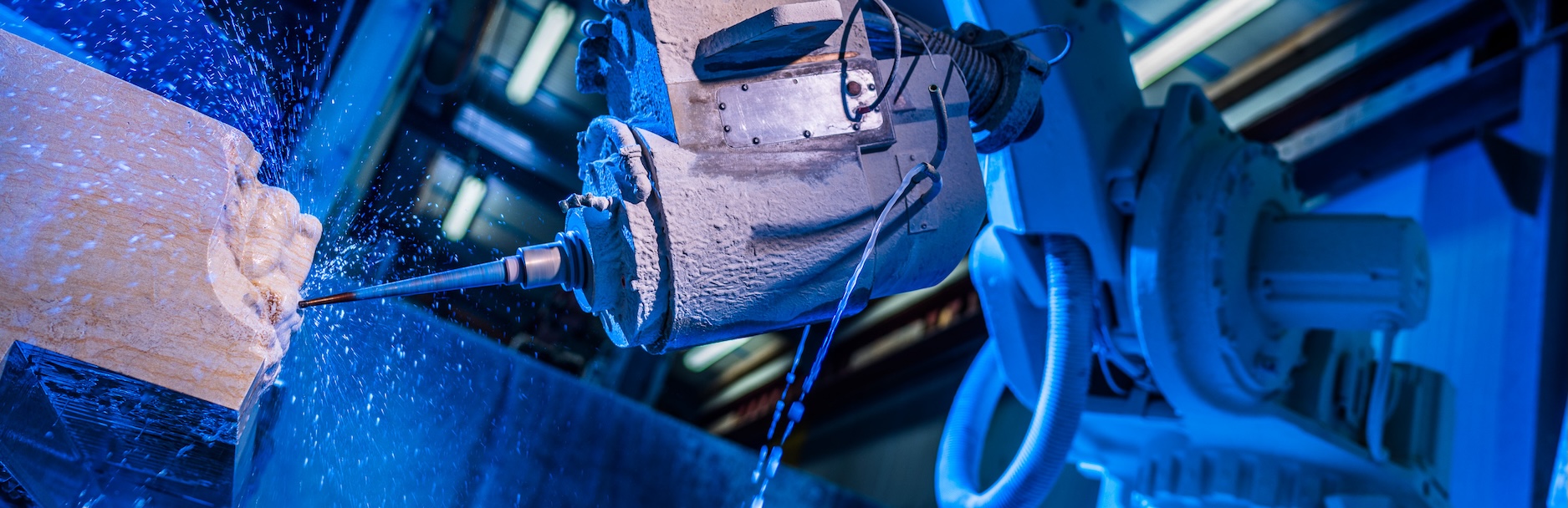 Ein Industrieroboter führt eine Bohrarbeit an einem Werkstück aus, aufgenommen in blauer Beleuchtung. Die Szene zeigt moderne Fertigungstechnologie in einem Steinmetzbetrieb.