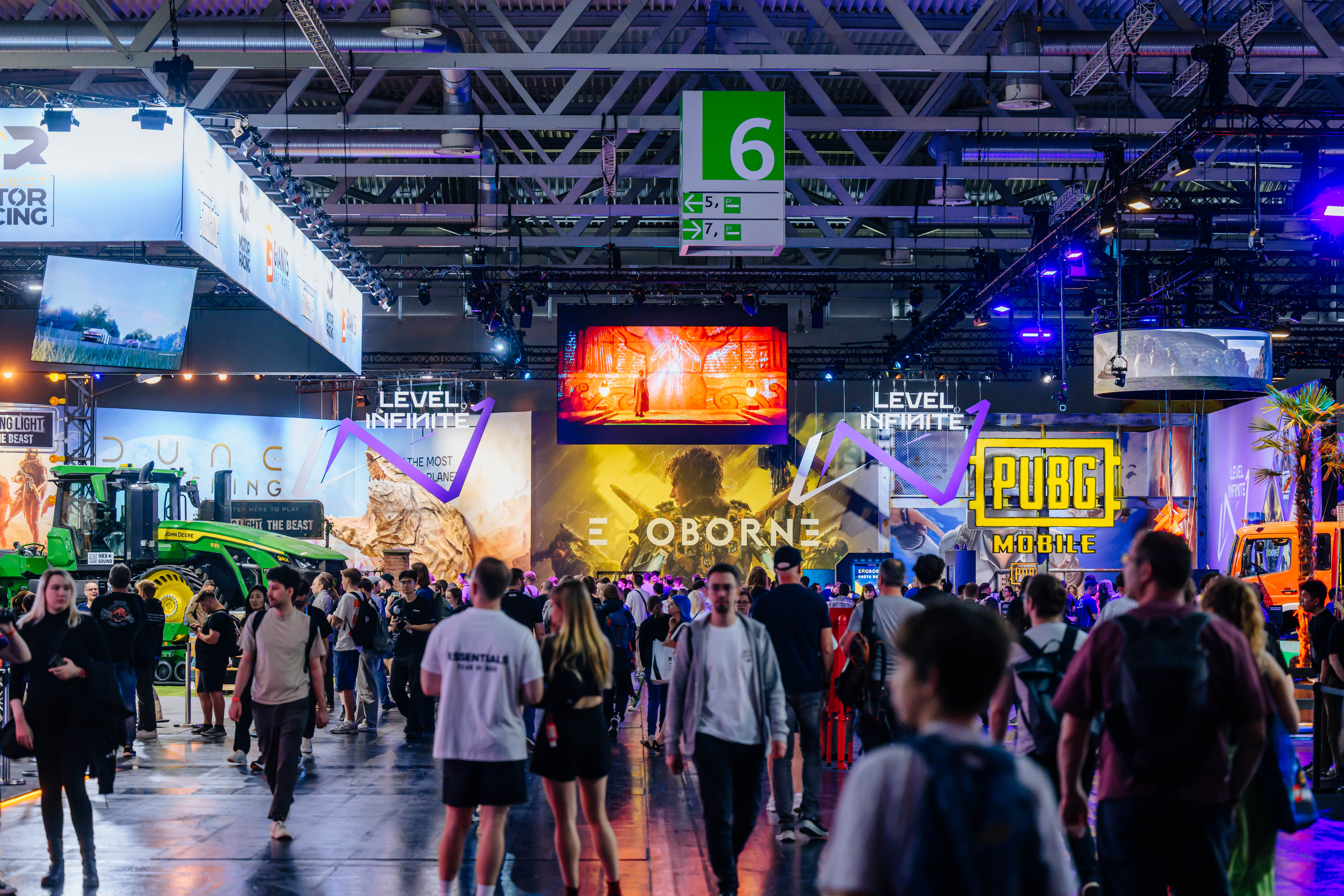 Zahlreiche Besucher gehen durch eine große Messehalle mit beleuchteten Ausstellungsständen für Videospiele wie "Level Infinite", "Eoborne" und "PUBG Mobile". An der Decke hängen Wegweiser für Halle 6 sowie Monitore mit Spielinhalten.